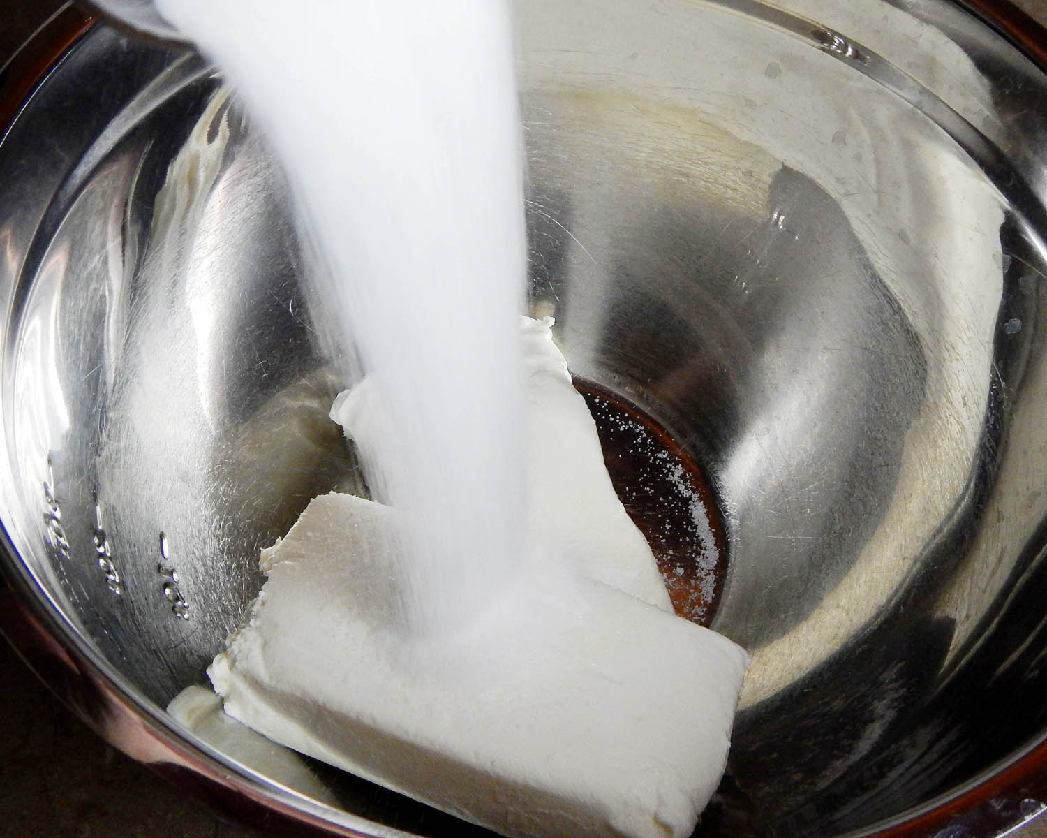 Pouring sugar on cream cheese for cheesecake
